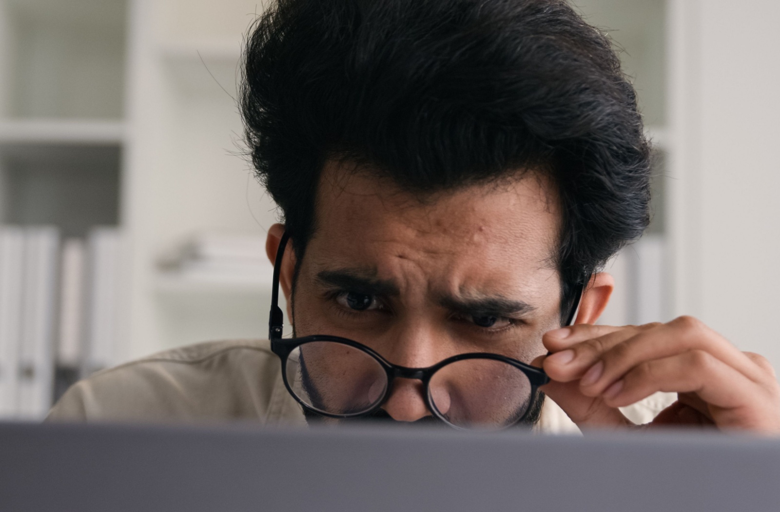 A tech worker pulls their eyeglasses down in an attempt to fix their blurry vision while working on a computer