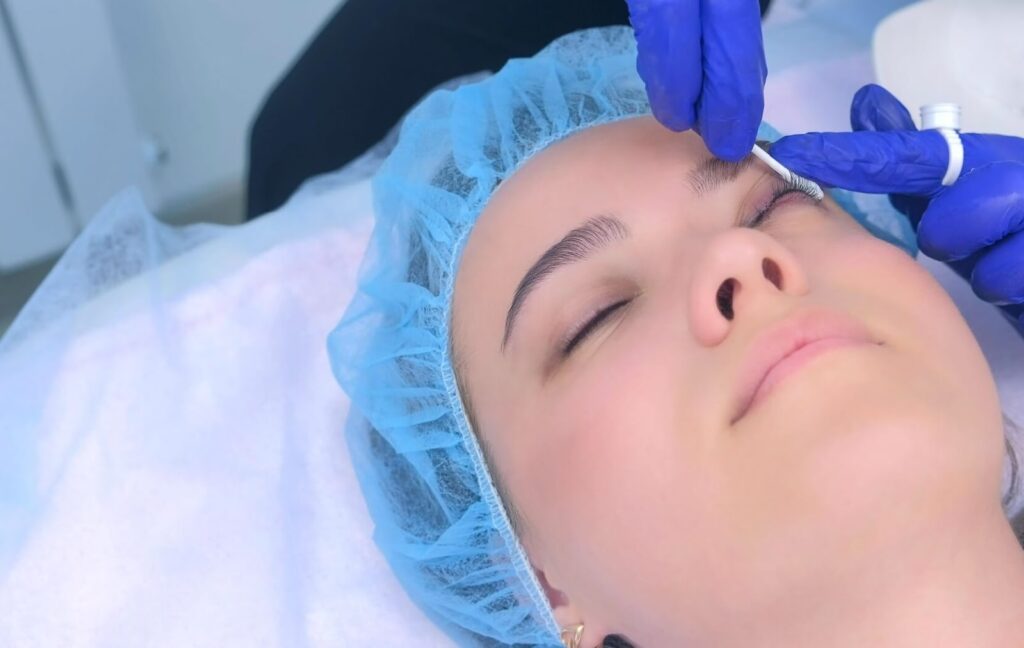 A patient lies back while an eye care professional uses a cotton swab to gently clean the patient's eyelids to help treat their blepharitis.