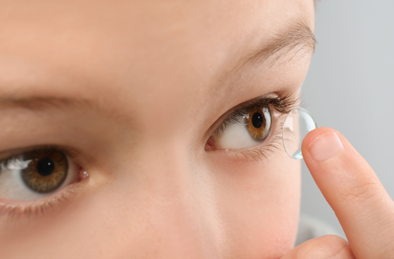 Close-up of a young child holding a contact lens near their eye to help slow the progression of myopia.