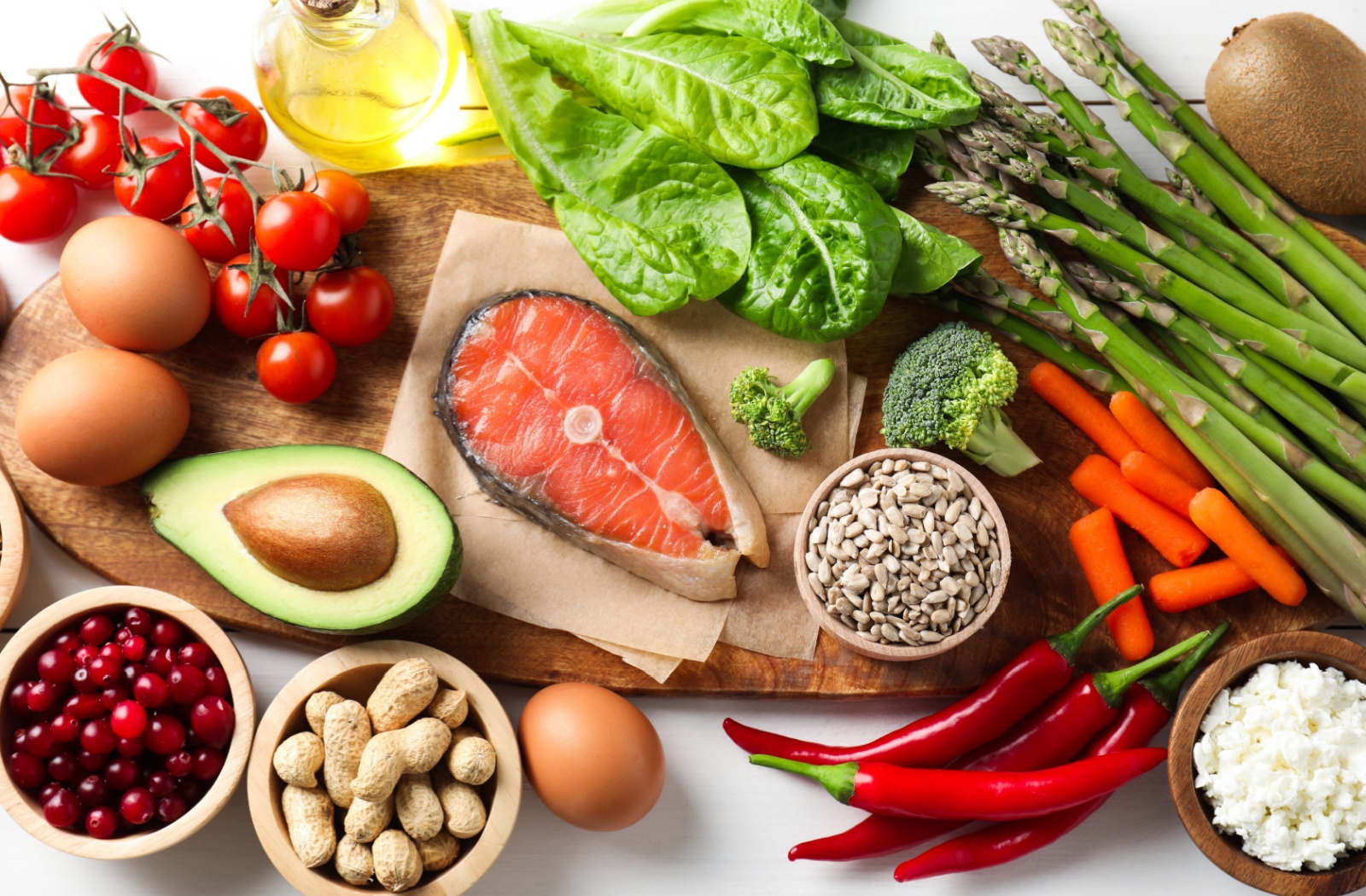 A variety of nutrient-rich foods that support eye health, including salmon, avocado, eggs, spinach, carrots, tomatoes, nuts, seeds, and olive oil, arranged on a wooden board.